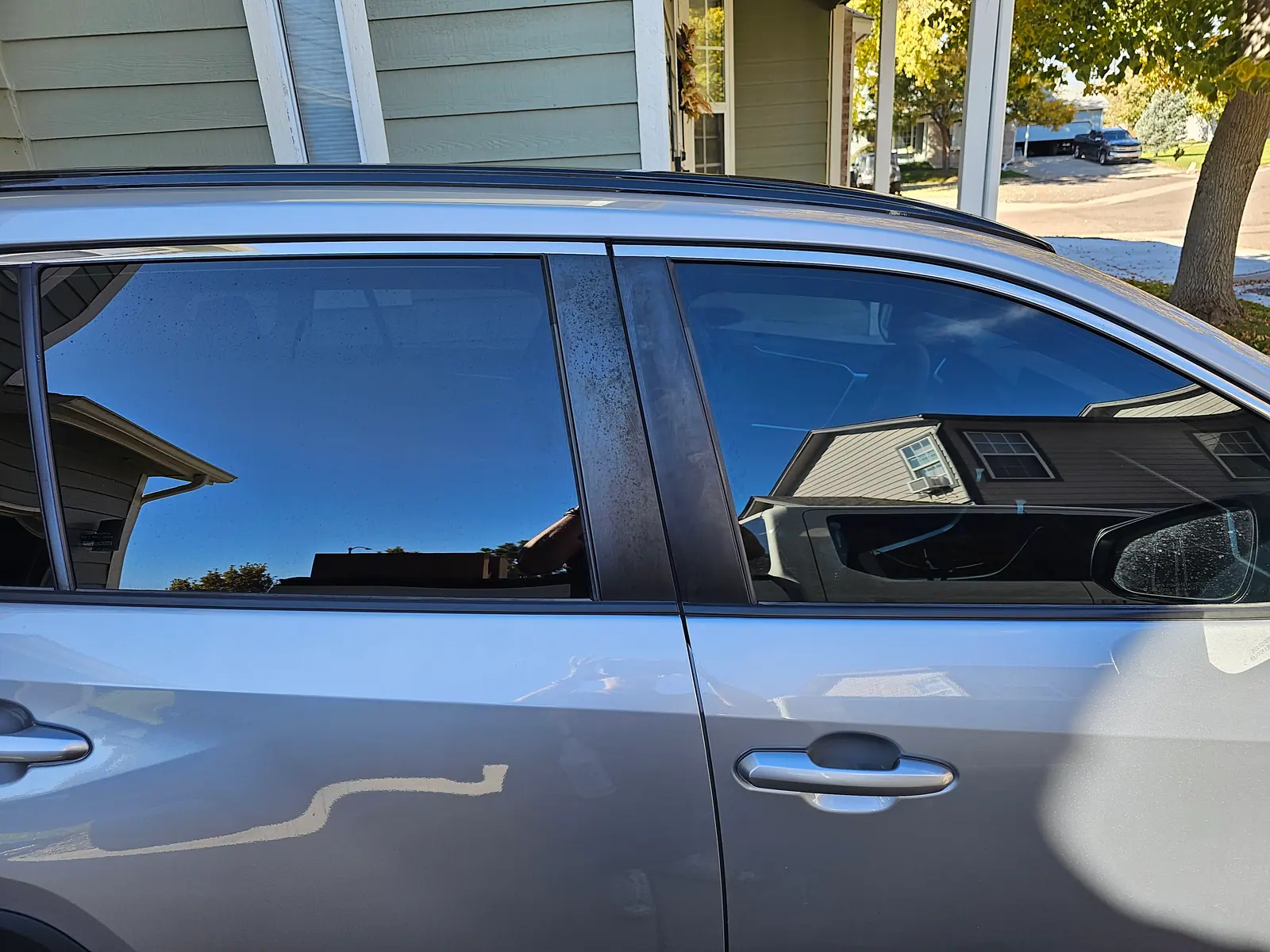 Freshly tinted front door glass on a silver car in a residential driveway